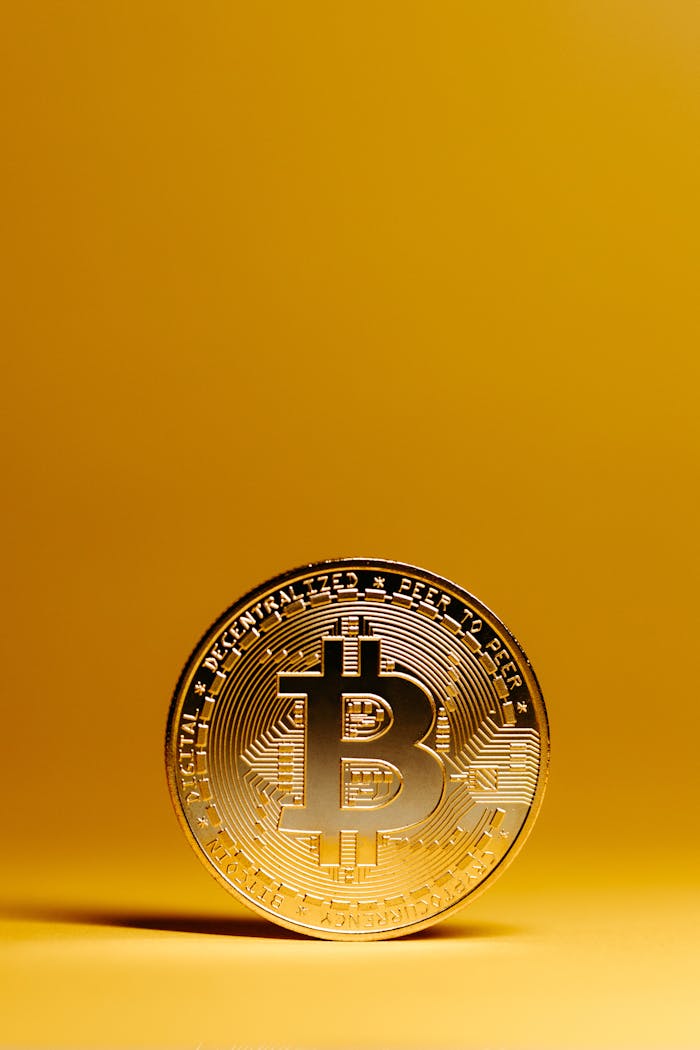 ours-journey A golden Bitcoin coin stands out against a vivid yellow background, representing digital currency and financial technology.