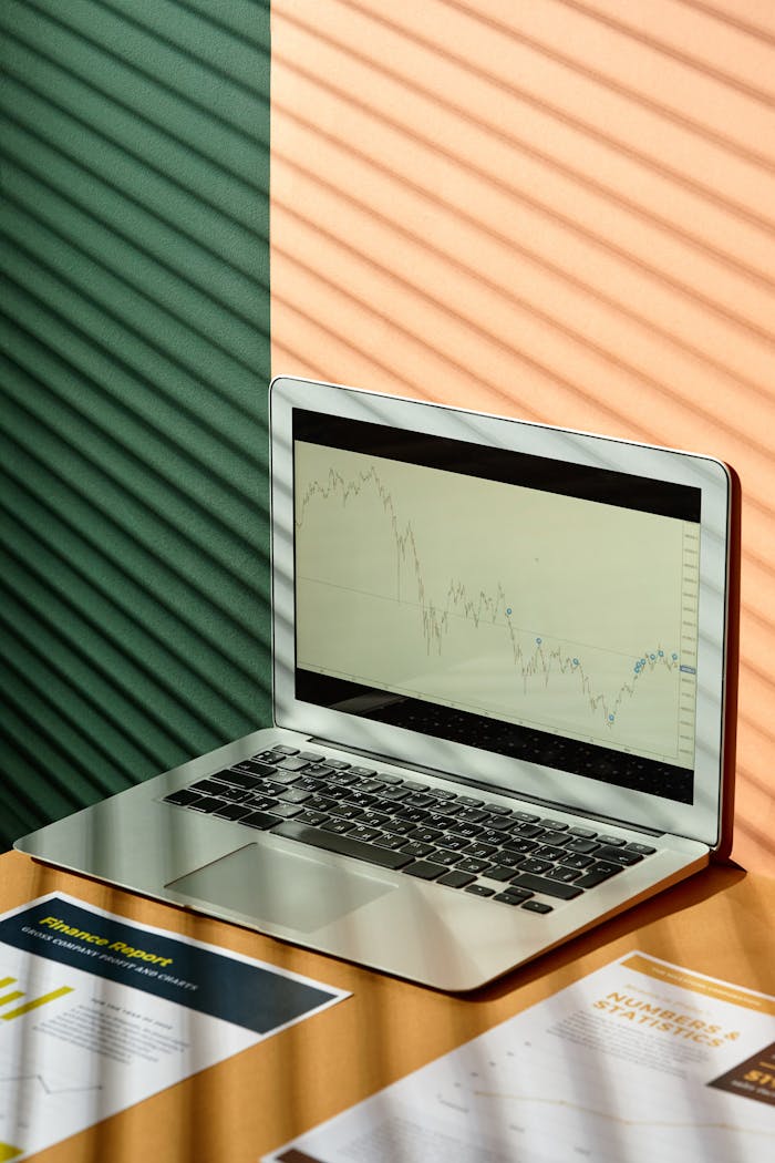 our-experience A laptop displaying financial graphs with documents on a sunlit office desk, ideal for finance themes.